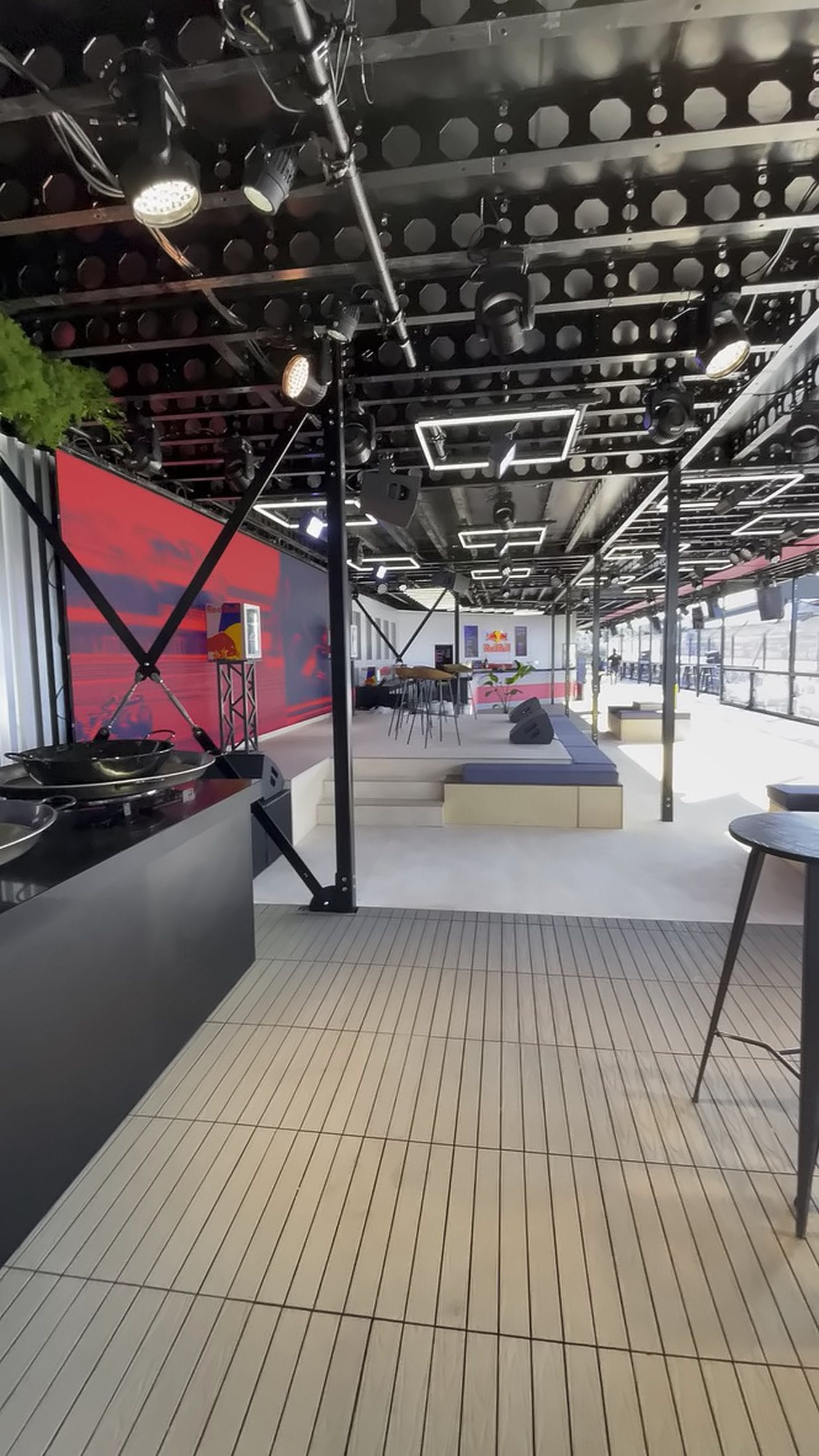 High-angle view of the Red Bull Pole Position hospitality suite, wood floor, branded bar and ceiling lighting, British Grand Prix 2025. Hover or tap to play a walkthrough.