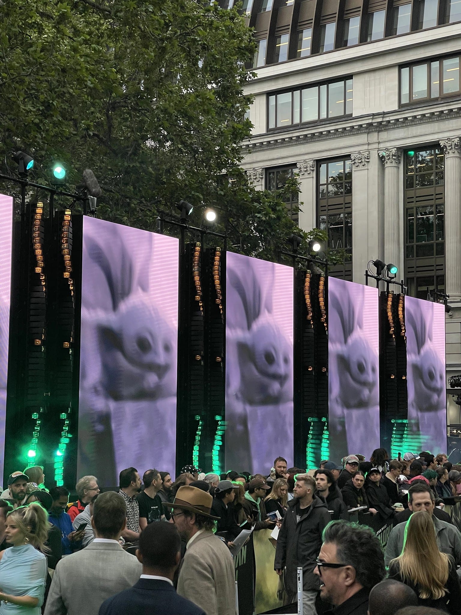 Four vertical LED panels showing Grogu, crowd in front, Leicester Square, May 2026.